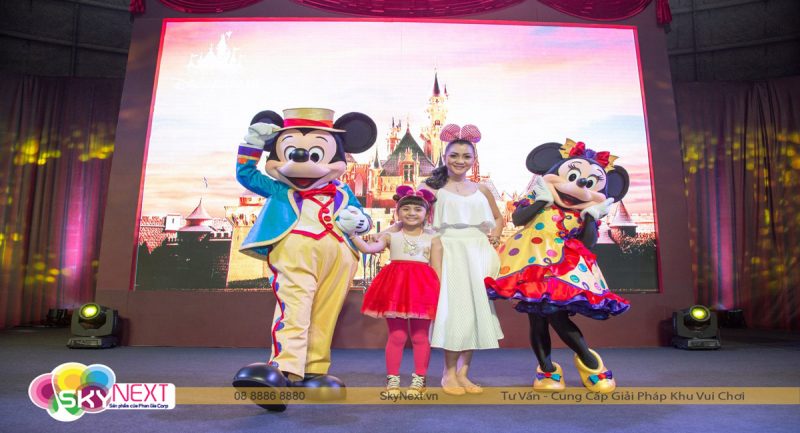 Mickey và Minnie đứng trên sân khấu cùng một phụ nữ và bé gái