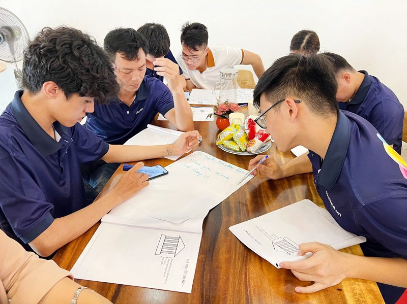 Nhóm kỹ thuật viên ngồi quanh bàn thảo luận bản vẽ và ghi chú